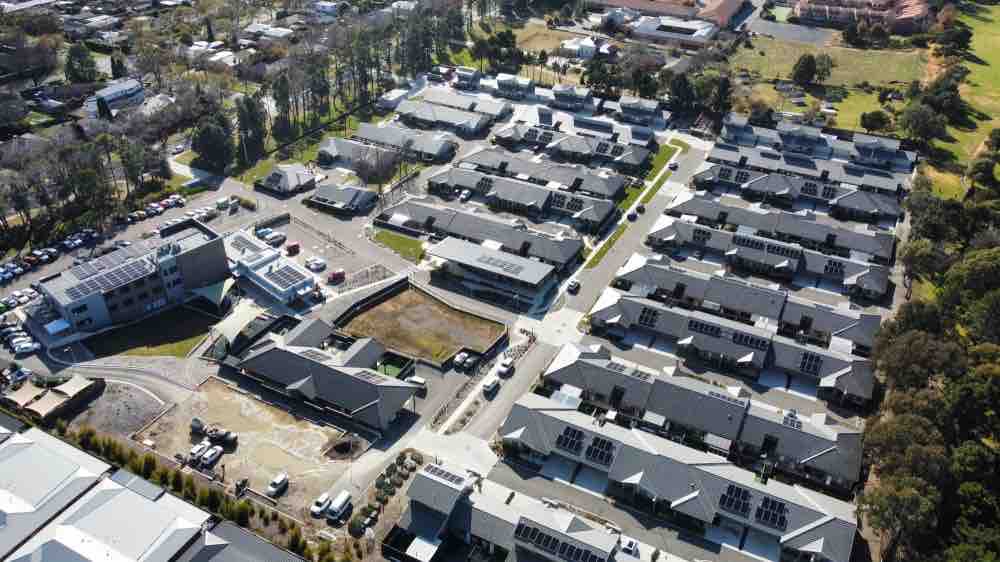 Aerial of the Marymead site in Canberra, rooftop solar spread across community buildings and a cluster of individual units